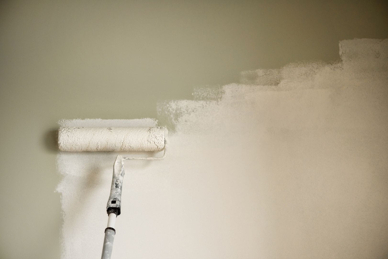 Gros plan d'un rouleau à peinture appliquant une teinte crème sur un mur intérieur en cours de finition.