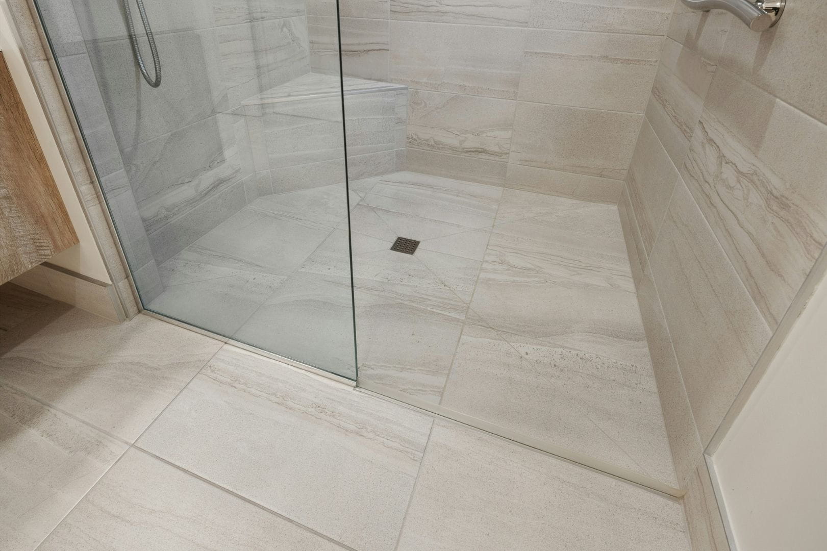 Pose de carrelage antidérapant dans une douche à l'italienne avec évacuation centrale et parois vitrées.
